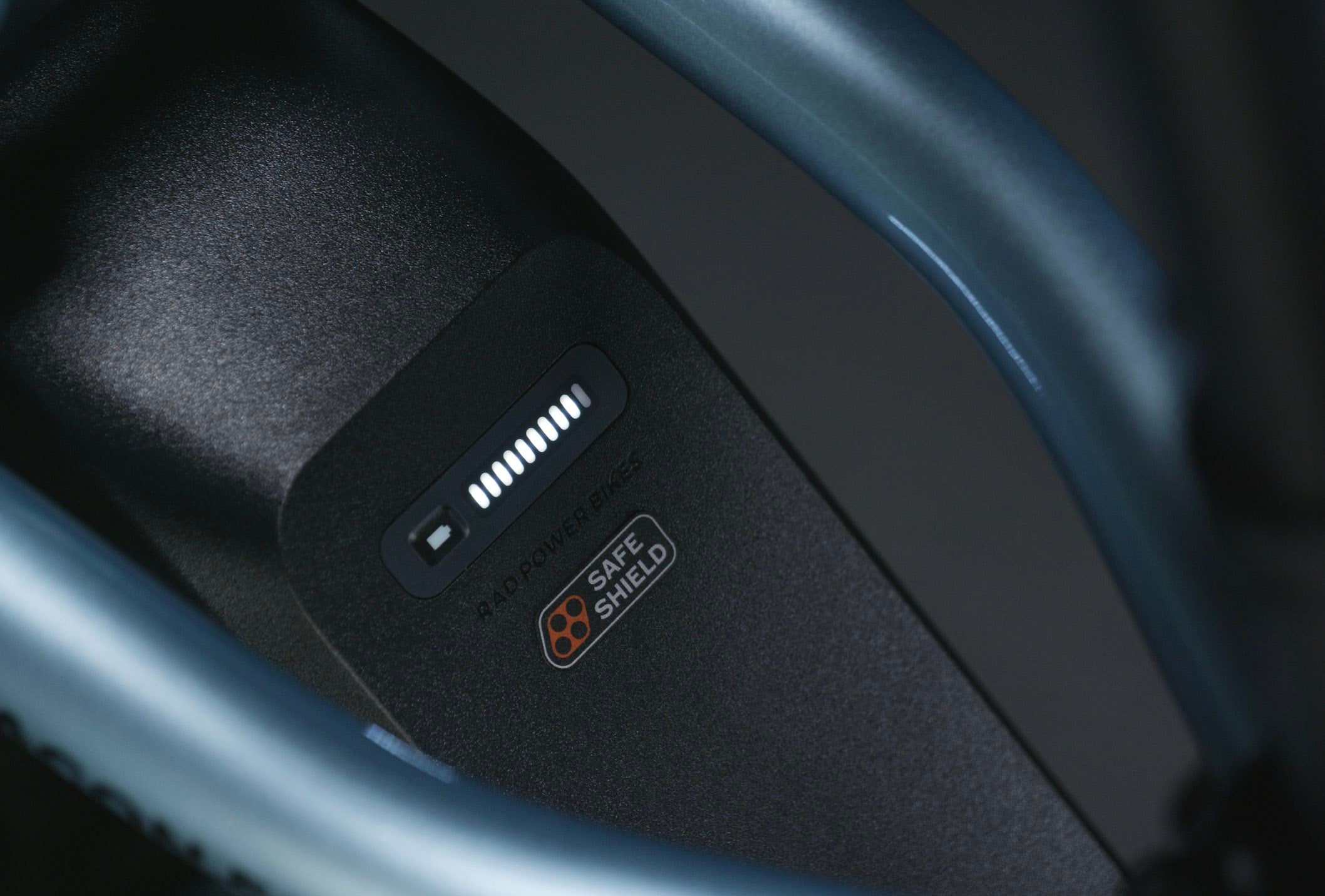 A close-up of a Safe Shield Battery on a blue bike in a dark studio setting.