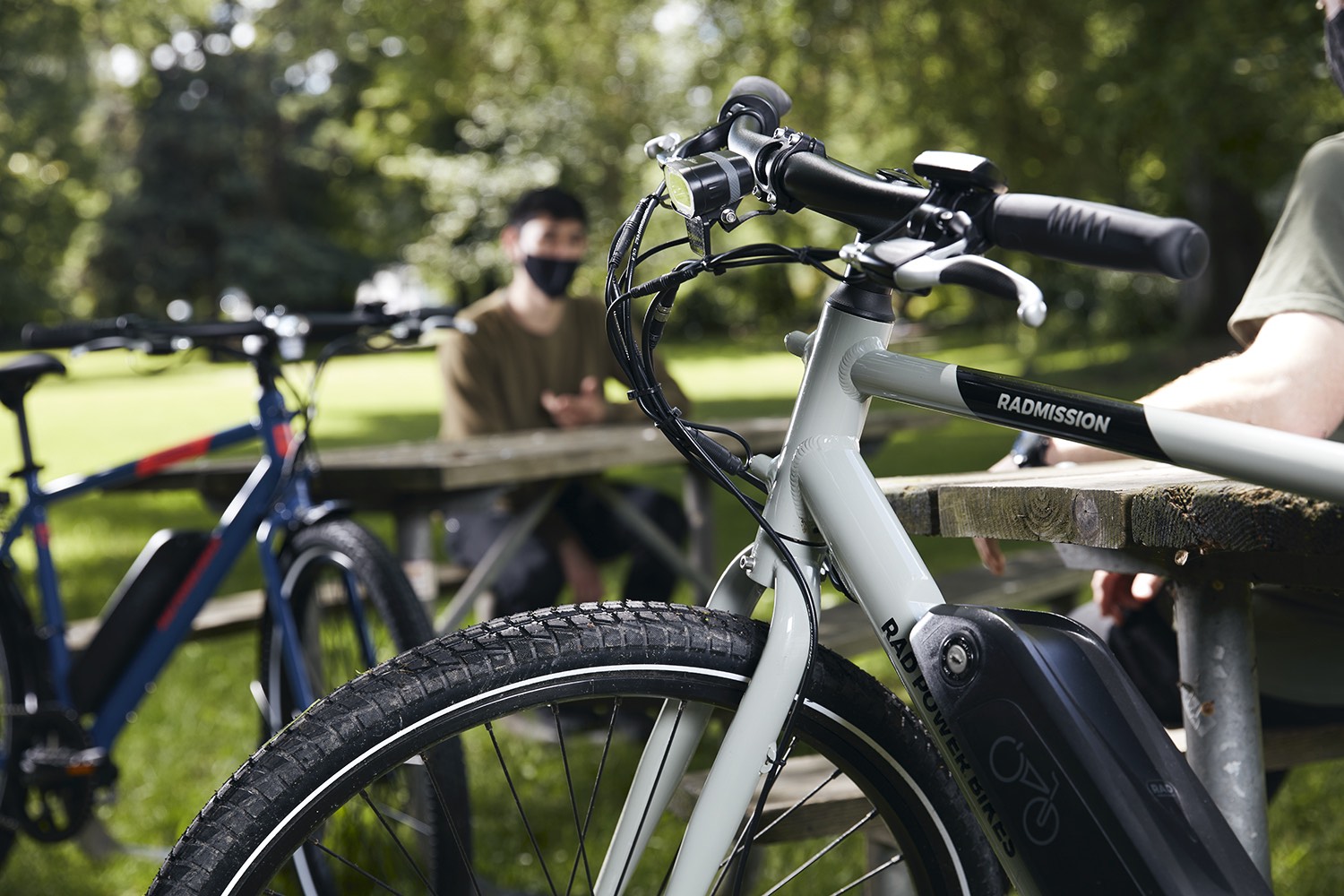 College students have a discussion at a park bench alongside their RadMission electric metro bikes