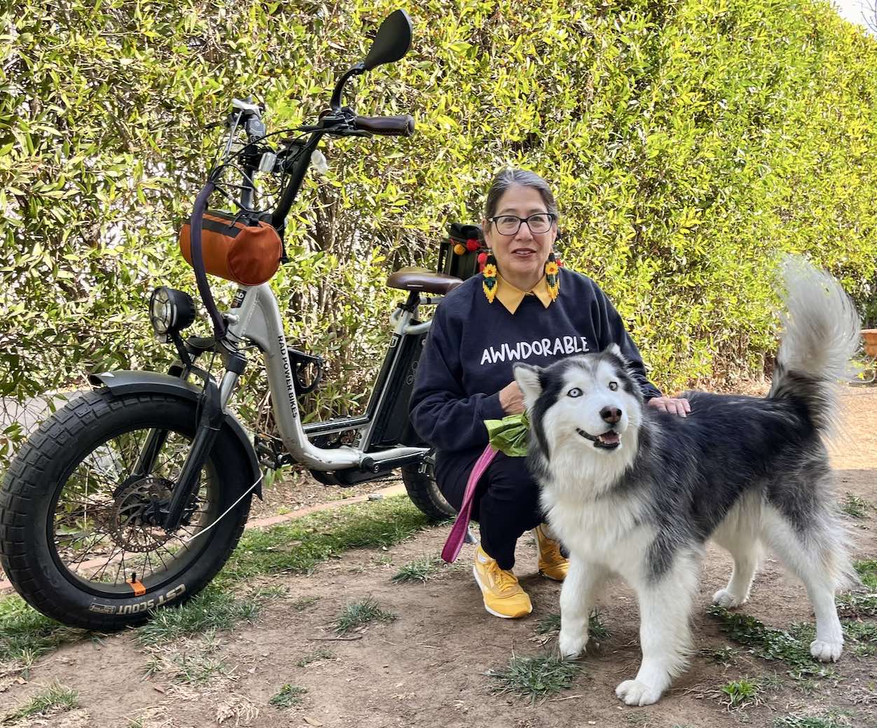 A woman poses alongside her RadRunner Plus in a sunny backyard with her black and white dog.
